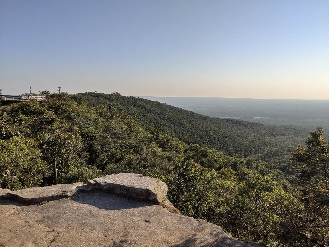 A scenic overlook of forested hills and a distant valley seen from a hiking trail viewpoint