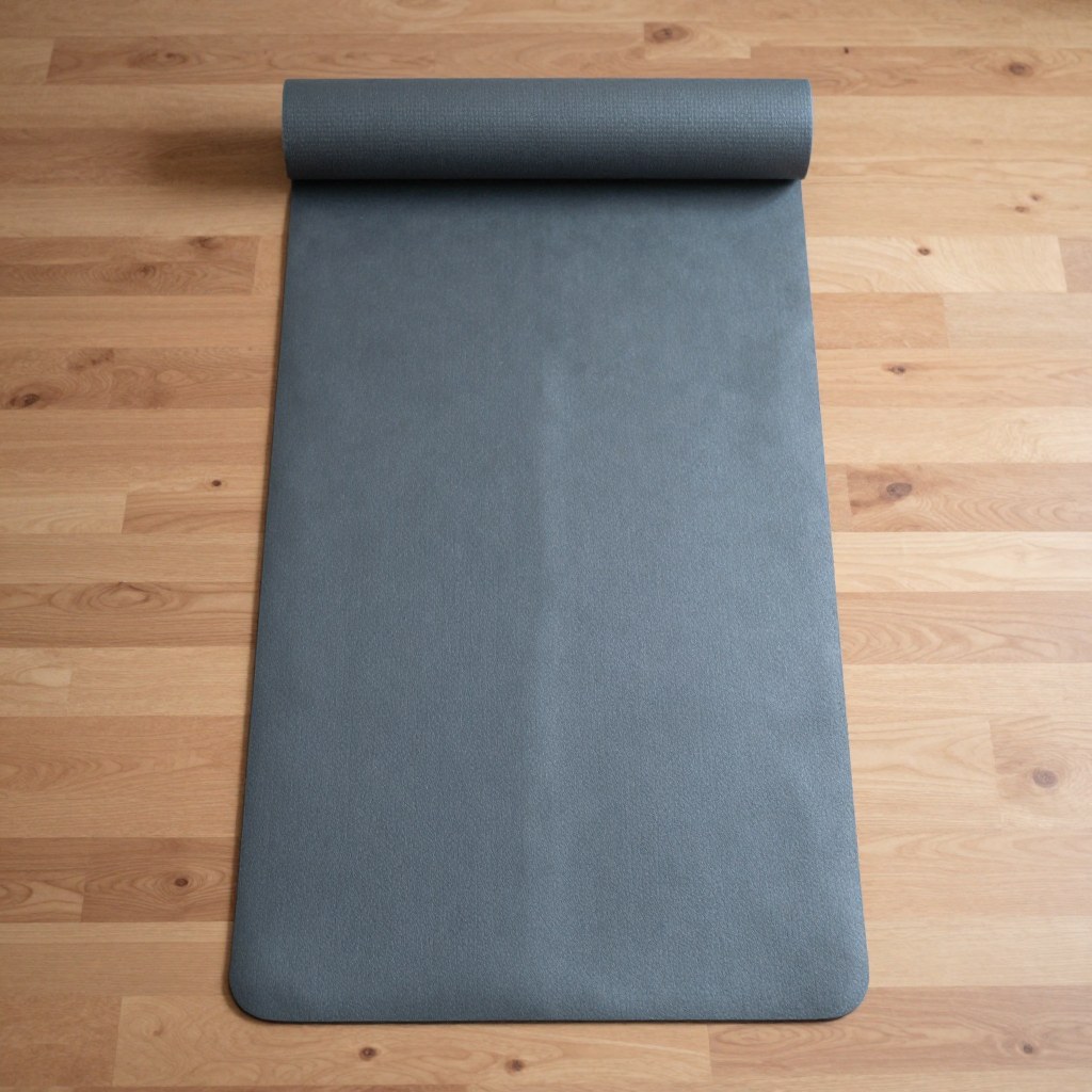 A single yoga mat unrolled flat and empty on the studio's wood-plank floor in front of the mirrored wall